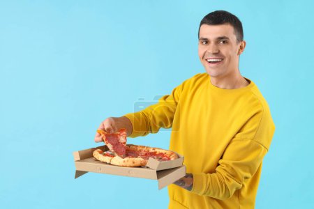 Photo for Young man with tasty pepperoni pizza on blue background - Royalty Free Image