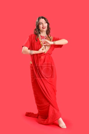 Téléchargez les photos : Belle jeune femme indienne en sari sur fond rouge - en image libre de droit