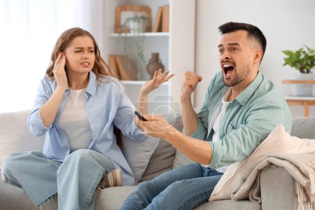 Young couple suffering from loud husband watching TV at home