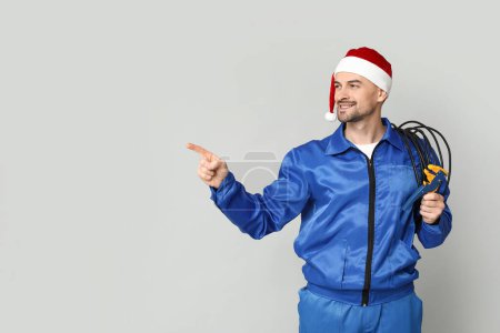 Foto de Retrato de electricista masculino en sombrero de Santa Claus con alambres y rizador apuntando a algo sobre fondo gris - Imagen libre de derechos