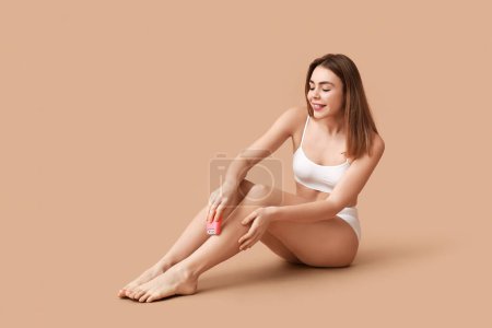 Photo for Beautiful young happy woman epilating her legs with modern epilator on brown background - Royalty Free Image