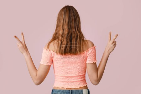 Photo for Pretty young woman showing peace gestures on pink background, back view - Royalty Free Image