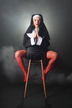 Sexy monja rezando en silla y humo sobre fondo oscuro