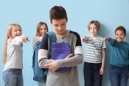 Photo for Bullied little boy with copybooks and pupils on blue background - Royalty Free Image