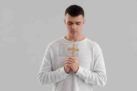 Foto de Joven con cruz de madera rezando sobre fondo gris - Imagen libre de derechos