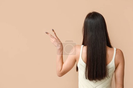 Photo for Young woman showing peace sign on beige background, back view - Royalty Free Image