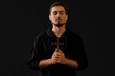 Foto de Joven con cruz de madera rezando sobre fondo negro - Imagen libre de derechos