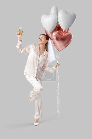 Happy bride in pajamas with champagne and balloons on light background. Hen Party