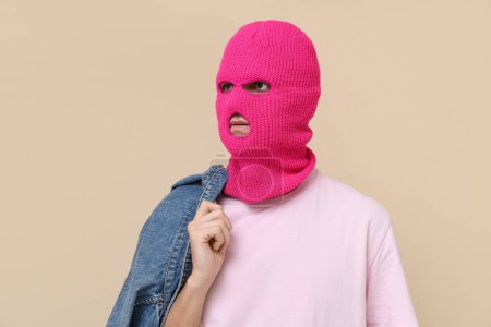 Handsome young man in balaclava with denim jacket on beige background