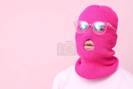 Schöner junger Mann in Sturmhaube mit stylischer Brille auf rosa Hintergrund