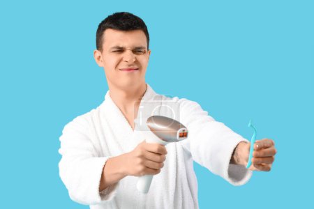 Photo for Young man choosing between photoepilation and shaving on blue background - Royalty Free Image