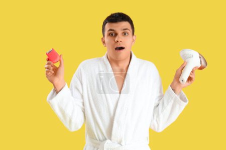 Surprised young man with different epilators on yellow background