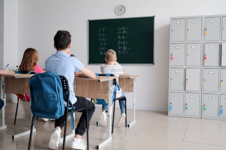 Téléchargez les photos : Petits élèves assis aux bureaux et casier dans la salle de classe, vue arrière - en image libre de droit