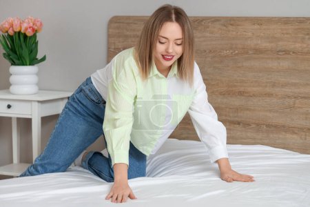 Photo for Pretty young woman making bed in bedroom - Royalty Free Image