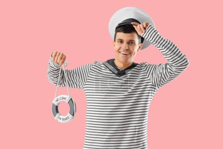 Young sailor with small ring buoy on pink background