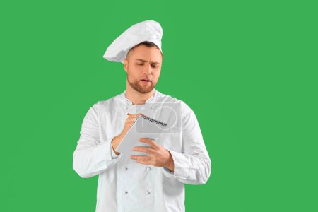 Male chef writing in notebook on green background. Reminder concept