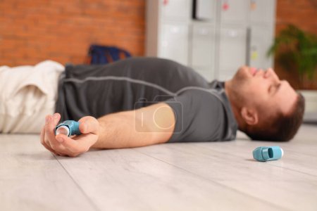 Téléchargez les photos : Jeune homme sportif avec inhalateurs couchés sur le sol dans la salle de gym, gros plan - en image libre de droit