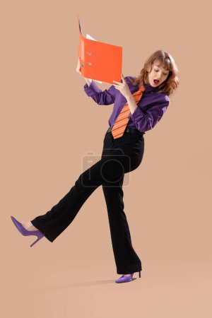 Foto de Divertido sorprendido joven mujer de negocios con carpeta sobre fondo marrón - Imagen libre de derechos