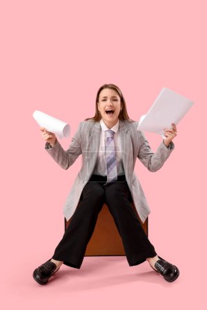 Foto de Joven empresaria divertida con documentos sentados en el maletín y gritando contra el fondo rosa - Imagen libre de derechos