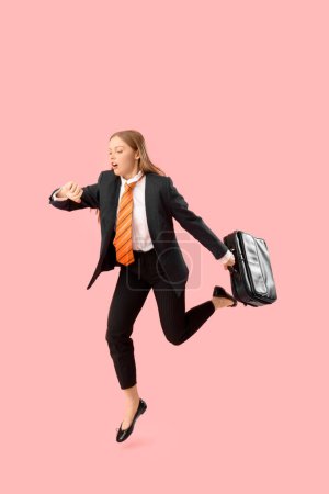 Foto de Divertida mujer de negocios con maletín saltando y tratando de cumplir la fecha límite en el fondo rosa - Imagen libre de derechos