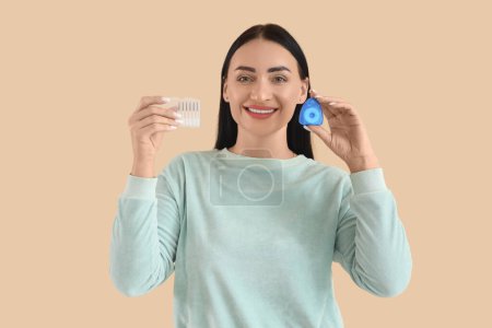 Téléchargez les photos : Belle jeune femme heureuse avec fil dentaire et mini brosses à dents sur fond beige - en image libre de droit