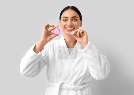 Téléchargez les photos : Belle jeune femme heureuse en peignoir avec fil dentaire sur fond gris - en image libre de droit