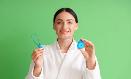 Téléchargez les photos : Belle jeune femme heureuse en peignoir avec fil dentaire et grattoir de langue sur fond vert - en image libre de droit