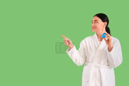 Téléchargez les photos : Belle jeune femme heureuse en peignoir avec fil dentaire pointant quelque chose sur fond vert - en image libre de droit