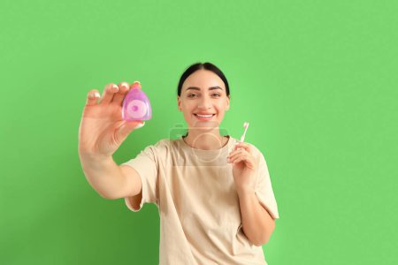 Téléchargez les photos : Belle jeune femme heureuse avec fil dentaire et brosse à dents sur fond vert - en image libre de droit