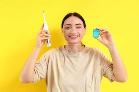 Téléchargez les photos : Belle jeune femme heureuse avec fil dentaire et brosse à dents électrique sur fond jaune - en image libre de droit