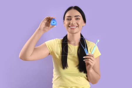 Téléchargez les photos : Belle jeune femme heureuse avec fil dentaire, brosse à dents et grattoir de langue sur fond violet - en image libre de droit