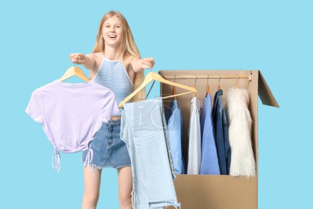 Foto de Hermosa mujer feliz joven y caja de armario con ropa sobre fondo azul - Imagen libre de derechos