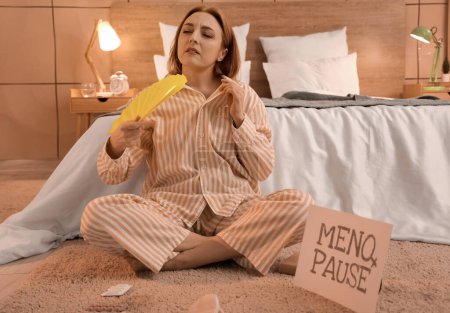 Mujer madura con ventilador que sufre de sofocos en el dormitorio por la noche. Concepto de menopausia