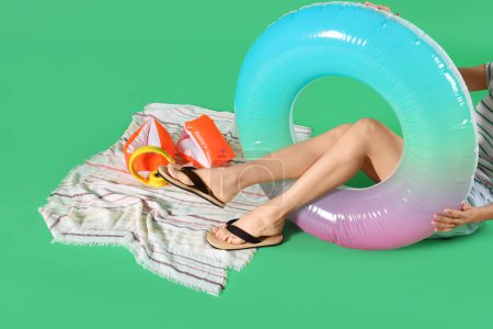 Young woman with inflatable ring, towel and headphones on green background. Summer holiday concept