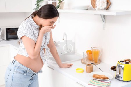 Téléchargez les photos : Jeune femme enceinte souffrant de toxicose dans la cuisine - en image libre de droit