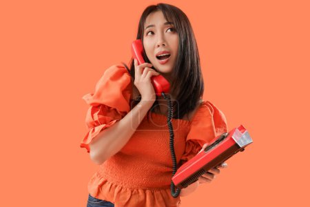 Young Asian woman talking with retro phone on orange background