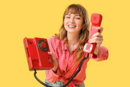 Young happy woman with retro phone on yellow background