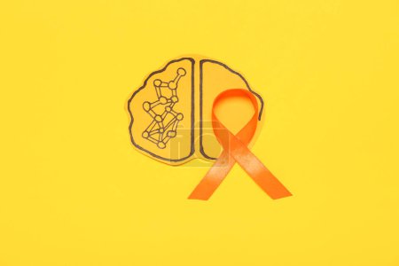 Cerebro de papel con cinta naranja sobre fondo amarillo. Mes de la conciencia de la esclerosis múltiple