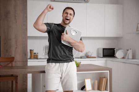 Téléchargez les photos : Heureux jeune homme sportif avec des balances dans la cuisine. Concept de perte de poids - en image libre de droit