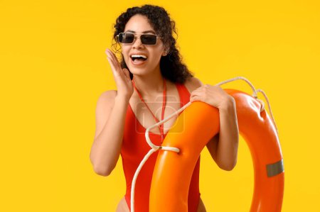 Photo for Beautiful young happy African-American female lifeguard with ring buoy on yellow background - Royalty Free Image