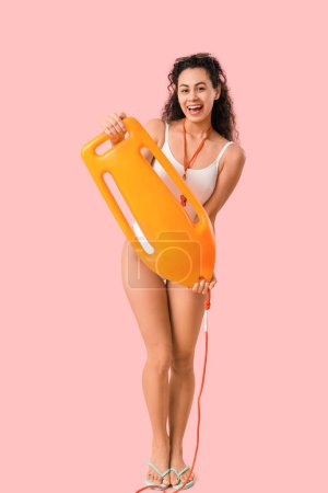 Beautiful young happy African-American female lifeguard with rescue buoy on pink background