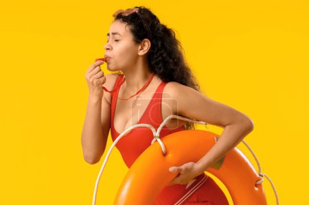 Photo for Beautiful young shocked African-American female lifeguard with ring buoy on yellow background - Royalty Free Image