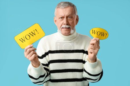Shocked senior man holding speech bubbles with word WOW on blue background
