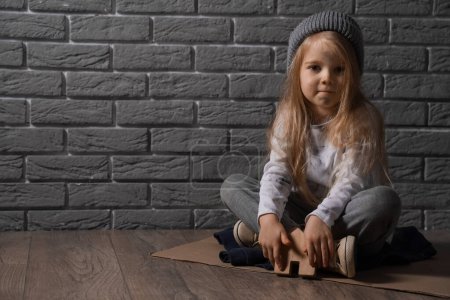 Photo for Homeless little girl with figure of house sitting near grey brick wall - Royalty Free Image