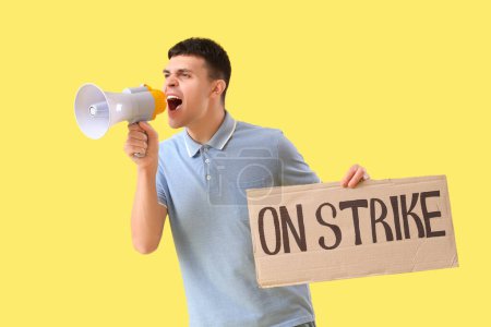Photo for Protesting young man holding placard with text ON STRIKE and shouting into megaphone against yellow background - Royalty Free Image