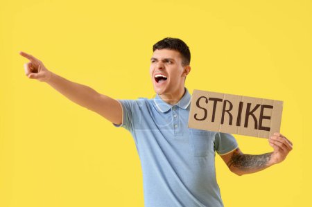 Photo for Protesting young man holding placard with word STRIKE pointing at something on yellow background - Royalty Free Image