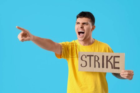 Photo for Protesting young man holding placard with word STRIKE and pointing at something on blue background - Royalty Free Image