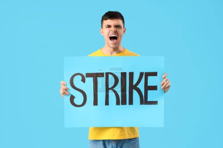 Photo for Protesting young man holding placard with word STRIKE on blue background - Royalty Free Image
