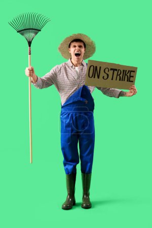 Protestando a un agricultor masculino sosteniendo pancarta con texto SOBRE STRIKE y rastrillo sobre fondo verde