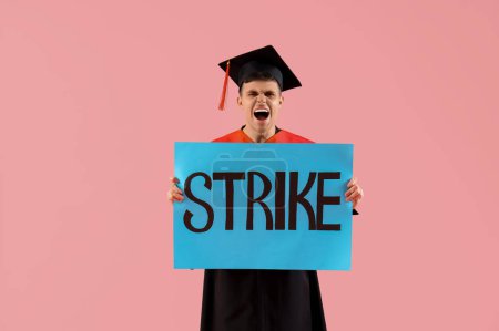 Protesting male graduate holding placard with word STRIKE on pink background